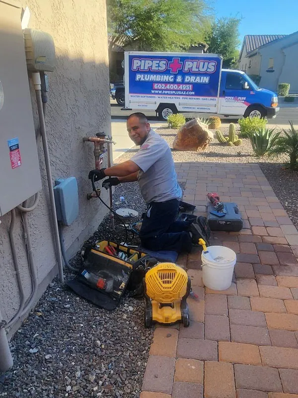 Plumber from Pipes Plus performing leak detection services outside a home, surrounded by tools and equipment, with a branded service vehicle in the background.